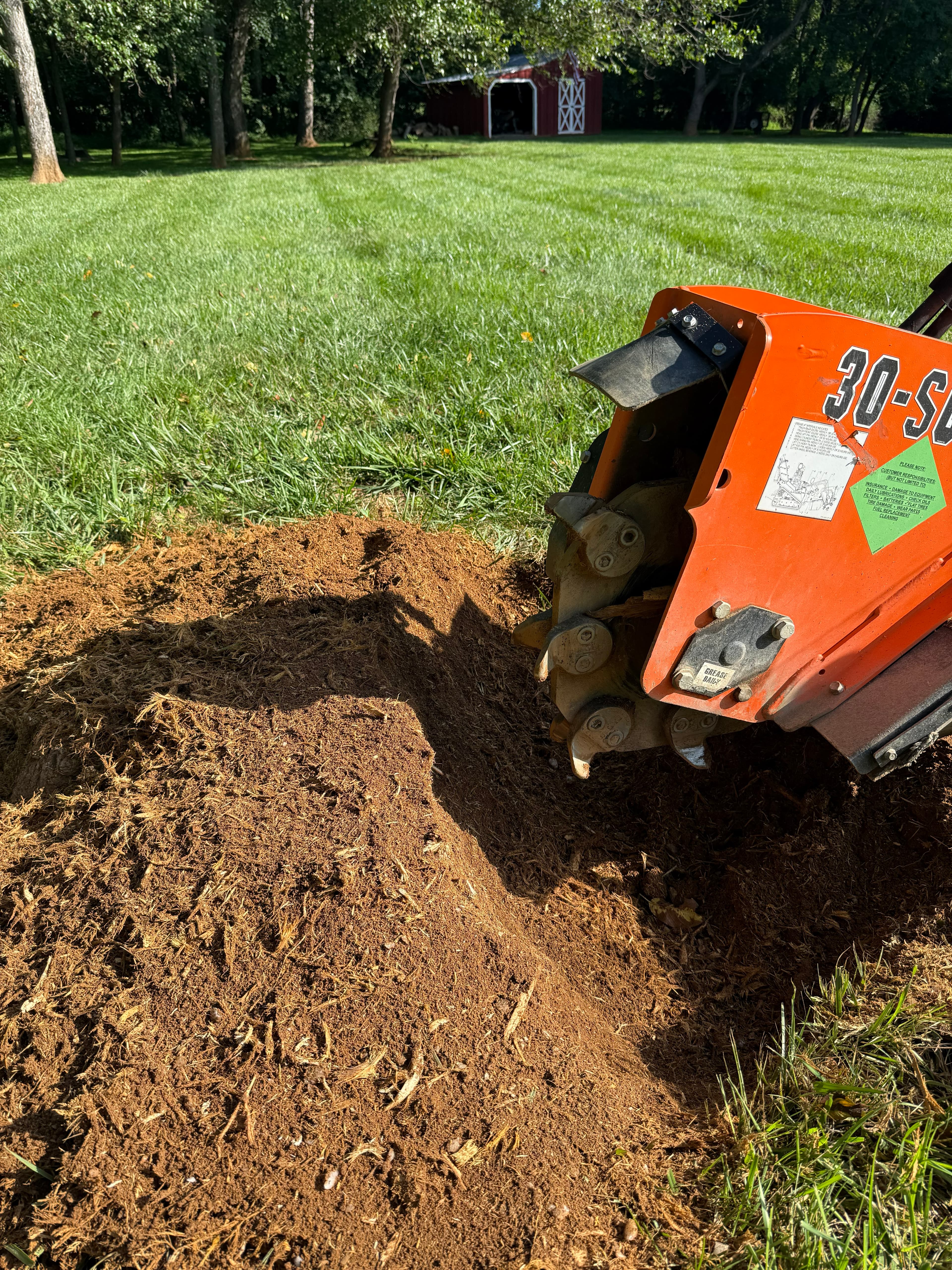 Orange stump grinder machine grinding a tree stump into a pile of wood chips.
